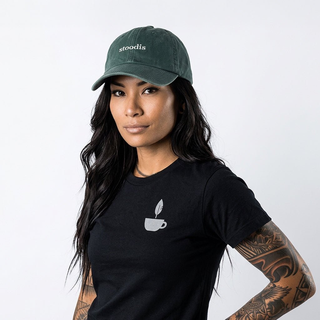 Woman wearing a black t-shirt with a logo and a green cap with 'stoodis' branding on a white background